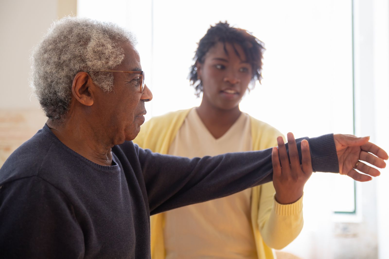 A Black woman professionally supporting an older adult at home.